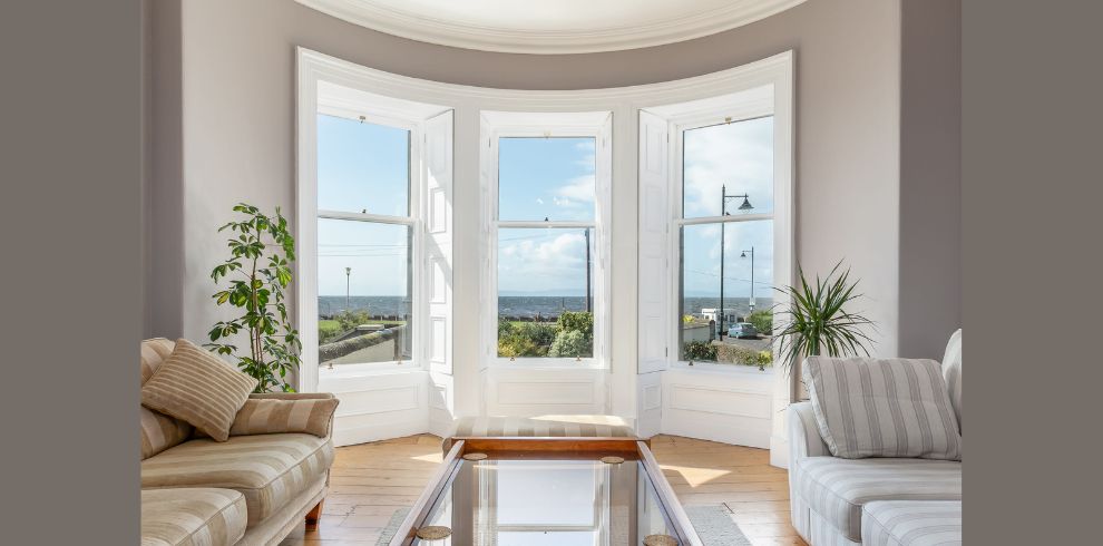 An image of a lounge seating area, with large bay windows with sunlight.