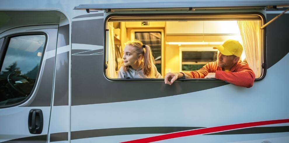 Girl and man looking out the window of a campervan.