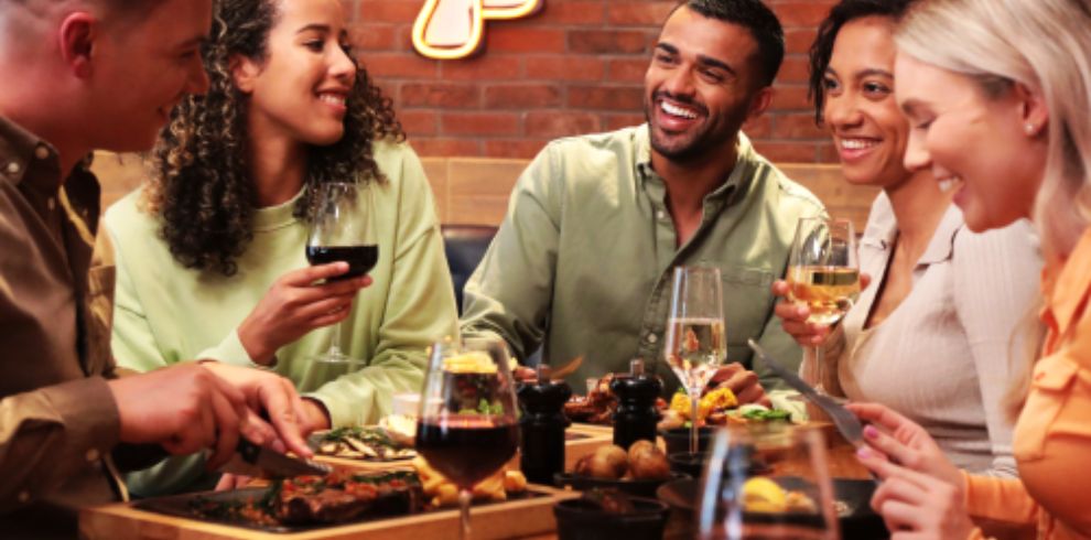 Group of adults sitting around a table having drinks and a meal.