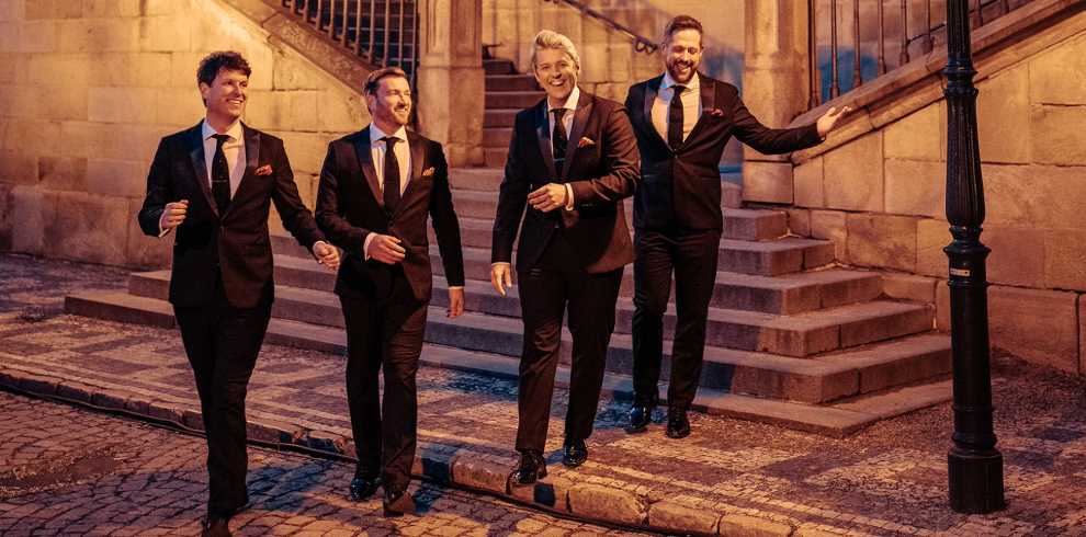 A group of men in black suits walking down a stair case outside.