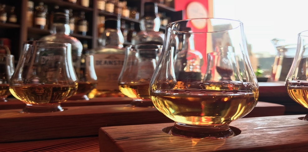 A picture of five glasses of whisky sitting on a table with bottles in the background.