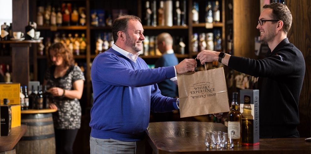 A man handing over a bag to a customer in the whisky shop