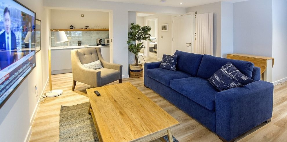 Modern living area with a blue sofa, cream chair and wooden coffee table
