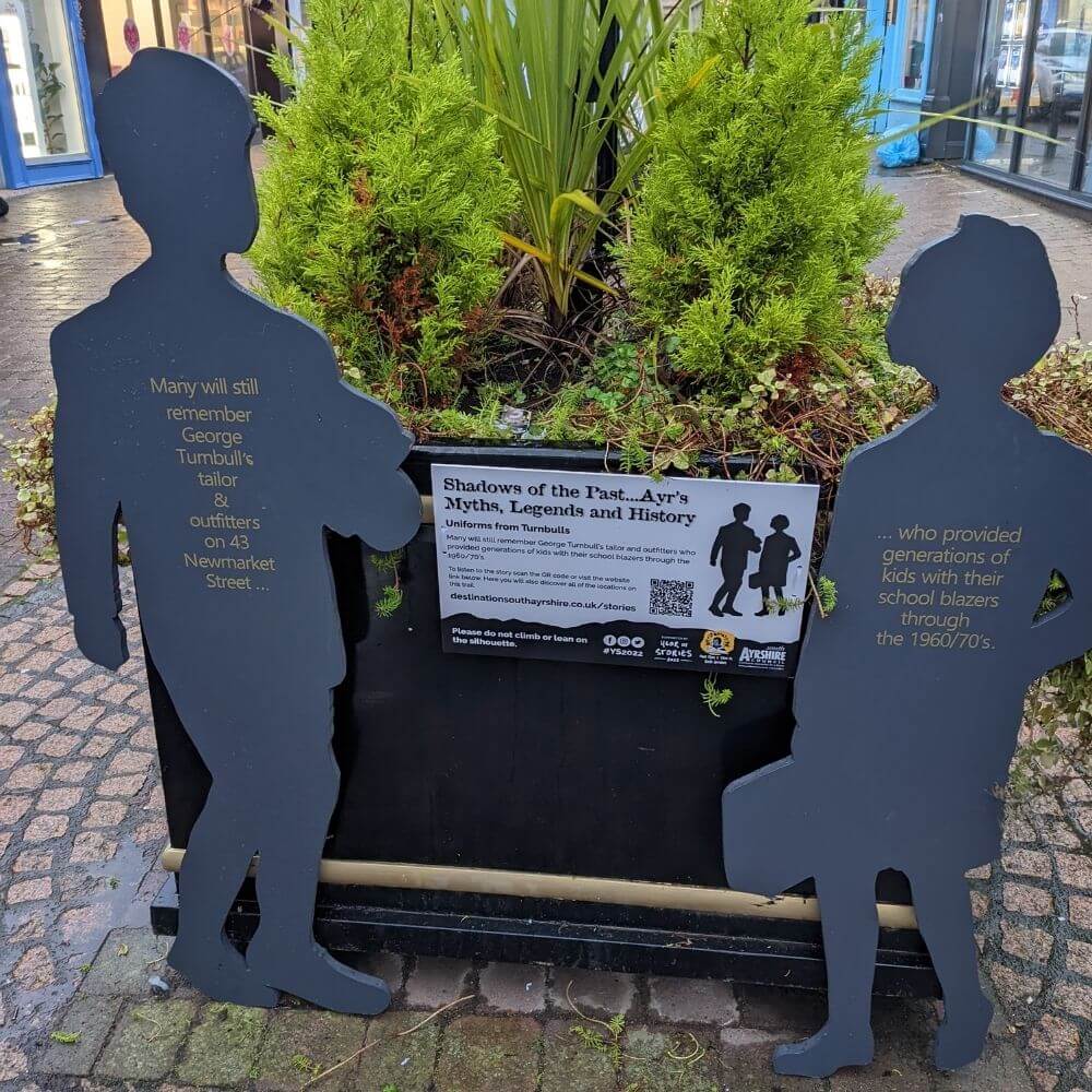 Wooden silhouettes of two children next to planter with green trees.