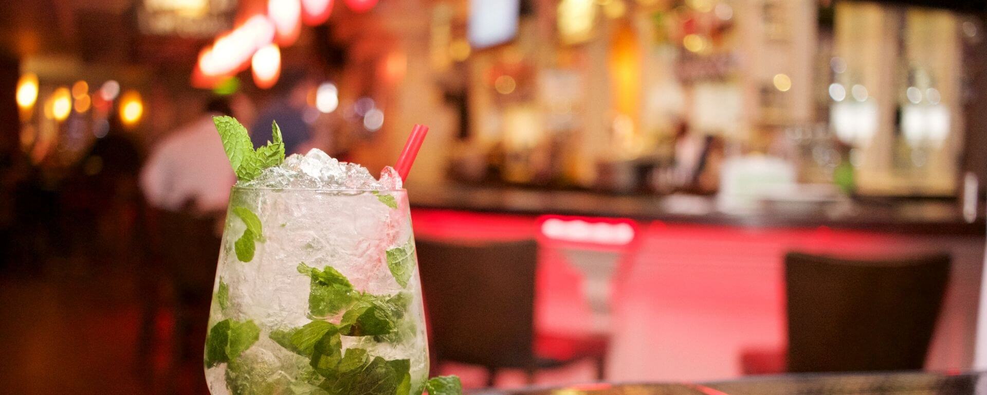Icy drink with mint leaves on a table with a bar in the background.