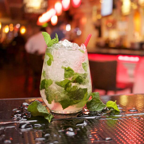 Icy drink with mint leaves on a table with a bar in the background.