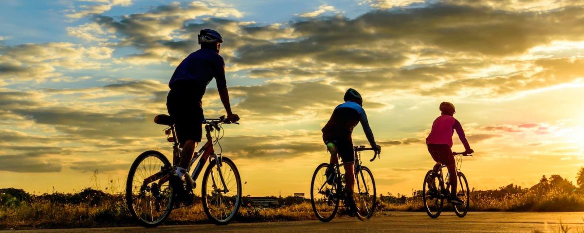 3 cyclists on a road at sunset.