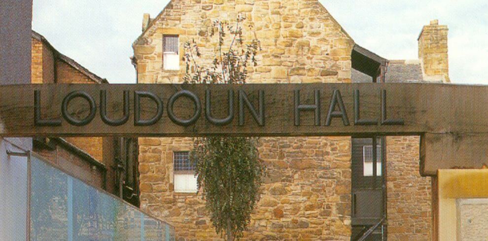 Wooden signage saying Loudoun Hall with stone townhouse dating to the early 16th century behind it.