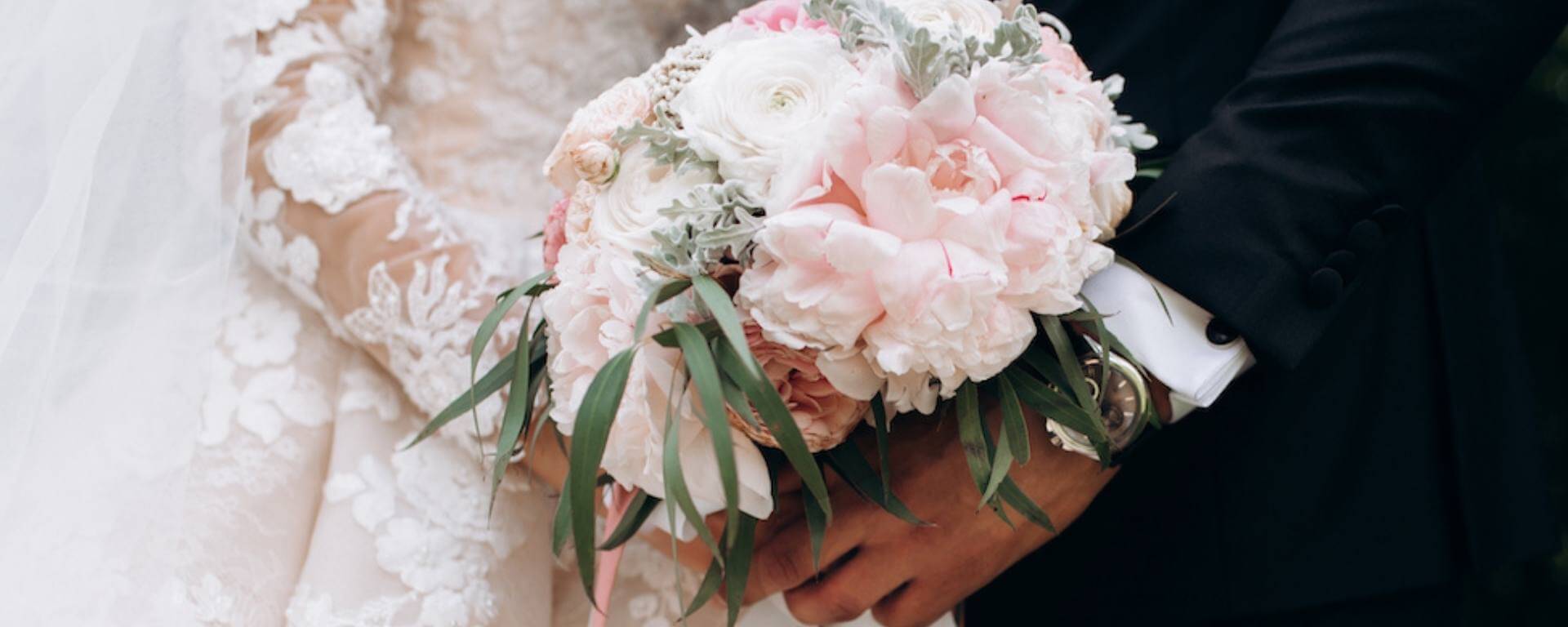 Front view of groom and brides hands together are holding wedding pink bouquet