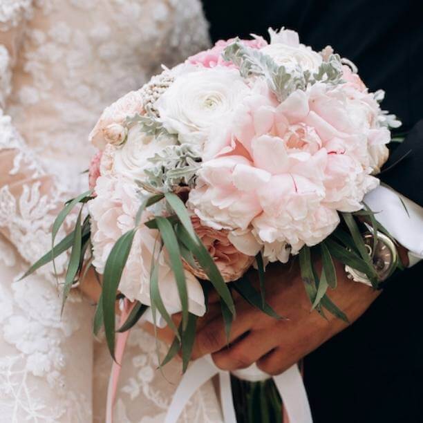 Front view of groom and brides hands together are holding wedding pink bouquet