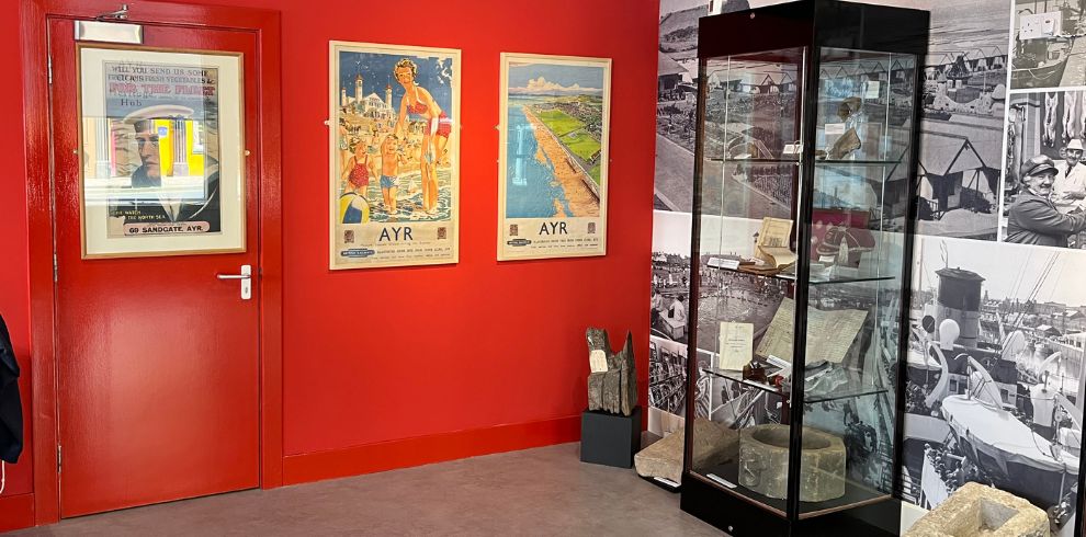 Bright red wall with old tourism posters. Glass cabinet with artefacts in front of a wall of old images.