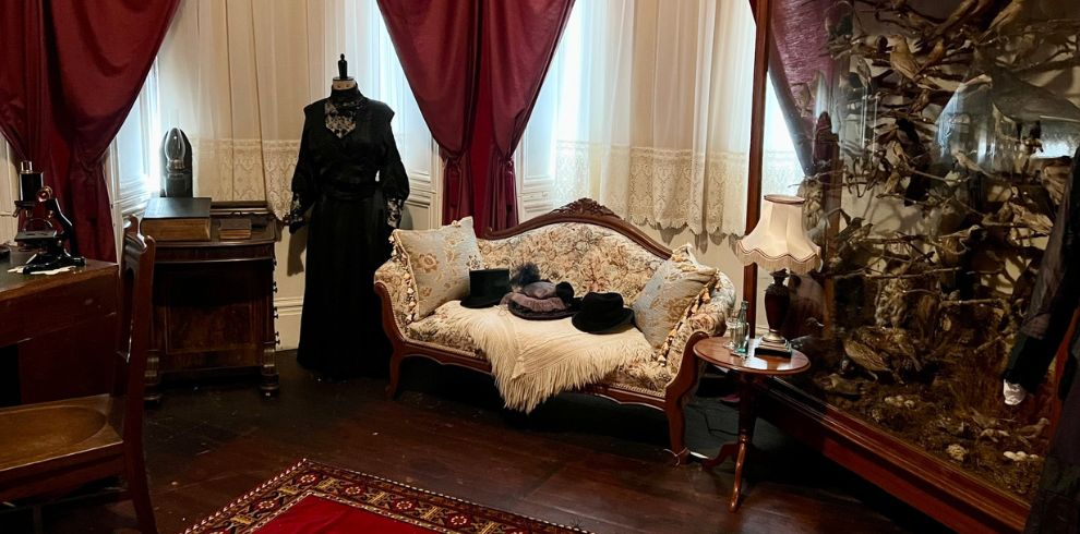 Room set up as a Victorian parlor with heavy red curtains and a cabinet of curiosities.