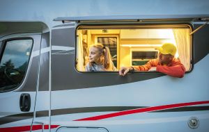 Young girl and man wearing a yellow hat looking out a motorhome window.
