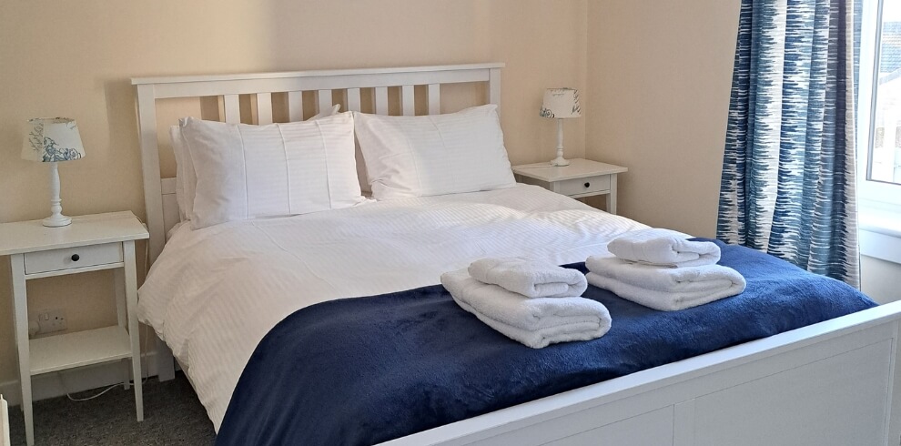 Cosy bedroom with white linen and blue throw.
