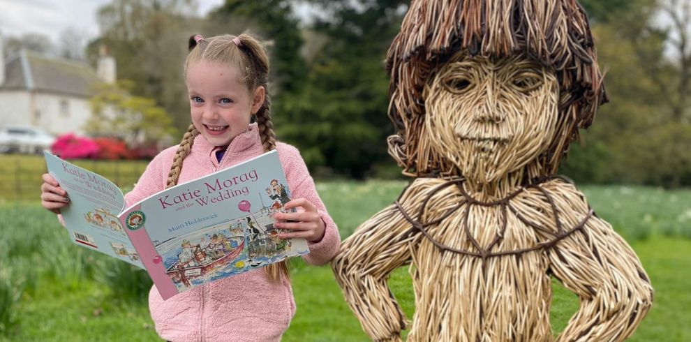 Young girl reading open book next to a willow sculpture.