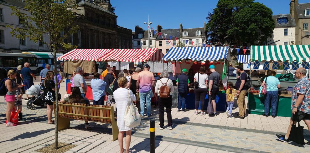 Bright sunny day on town square with busy market stalls.
