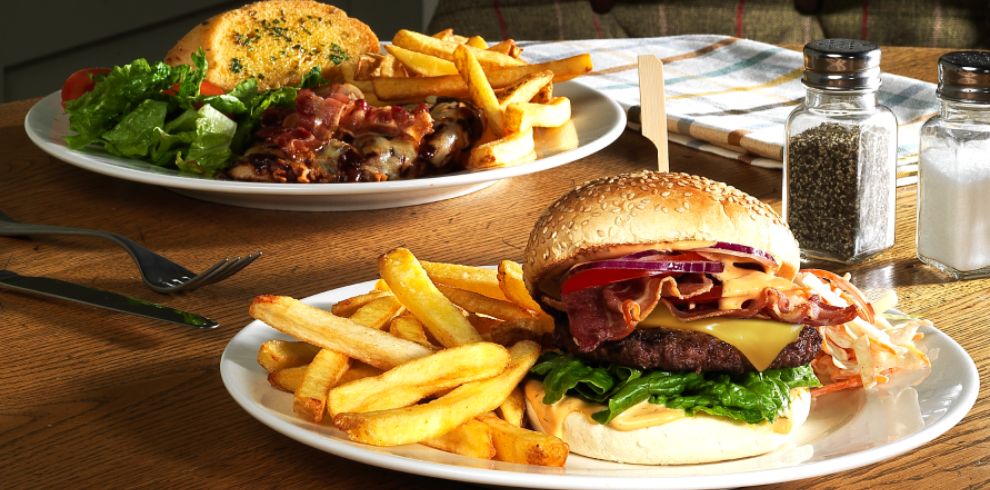 Table with two plates of delicious looking burgers topped with cheese and chips on the side.