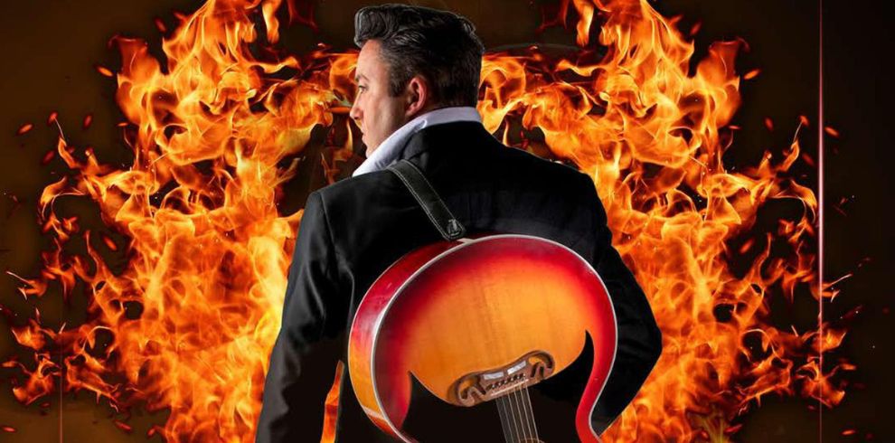 Man with guitar on his back with flames in front of him.