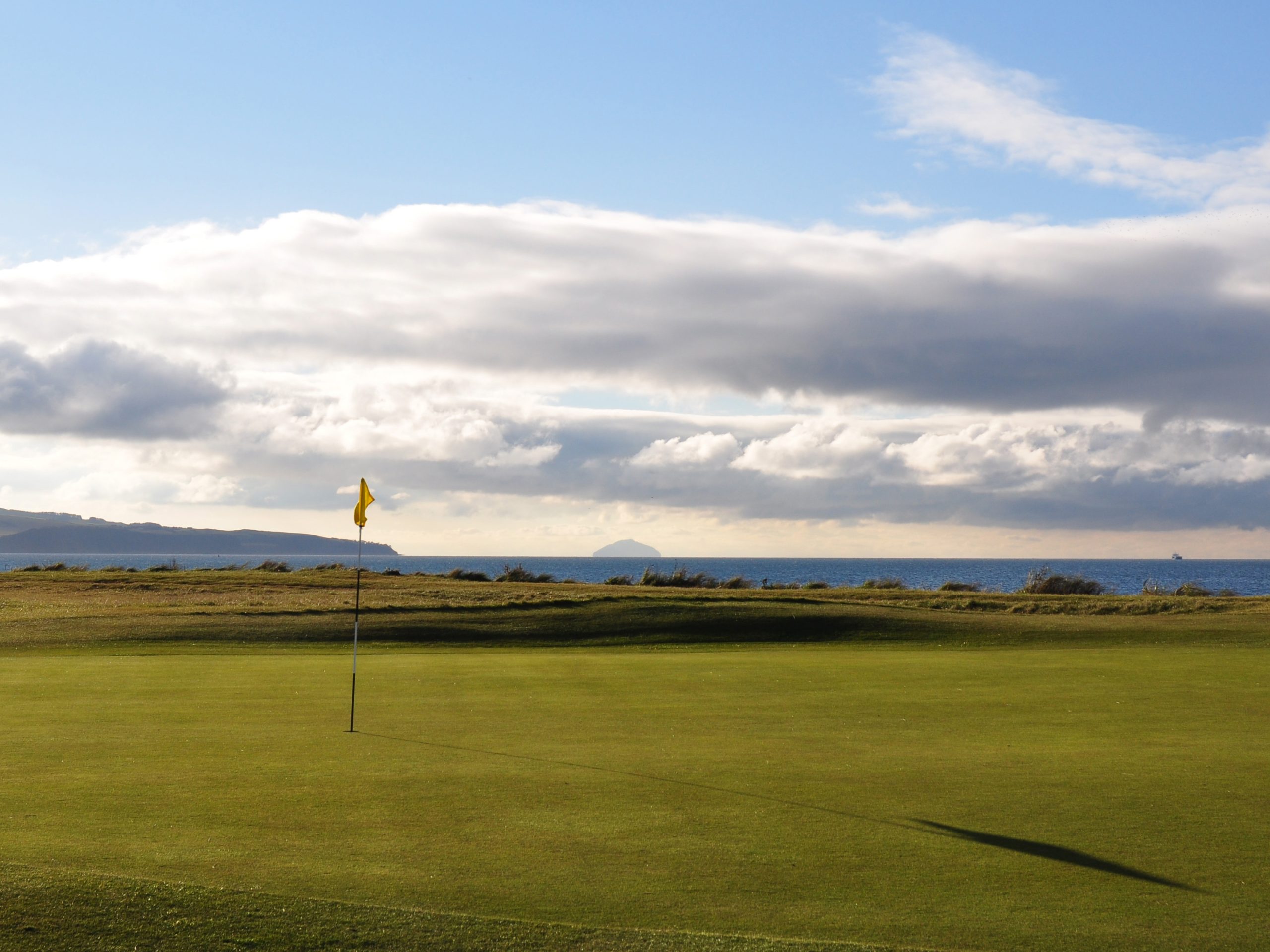 A photograph of the green at Prestwick St Nicholas Golf Club. In the background you can see the Ailsa Craig.