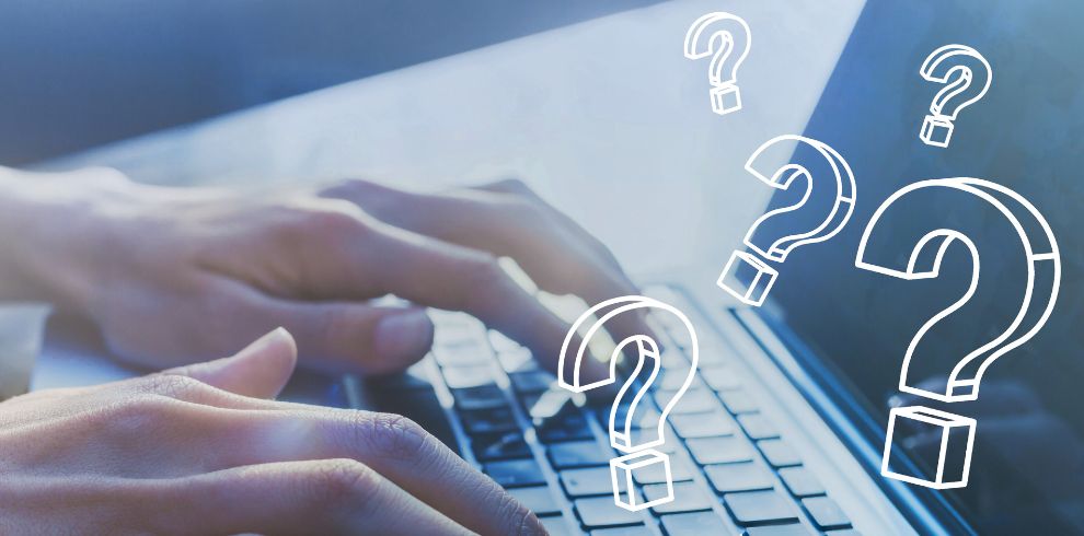 Hands typing on a keyboard with questions marks on screen.