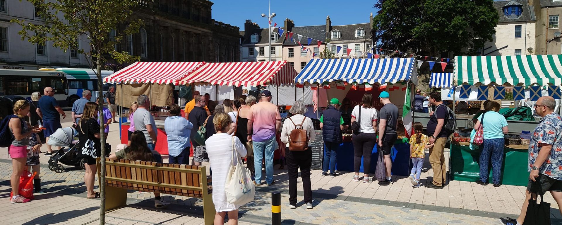 Bright sunny day on town square with busy market stalls.