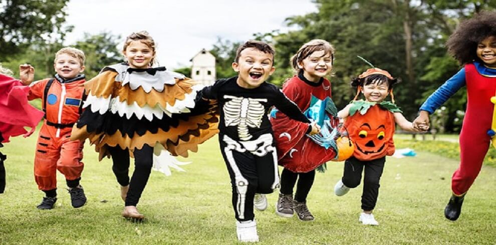 A group of children dressed up in Halloween costumes running outdoors with trees as a backdrop.