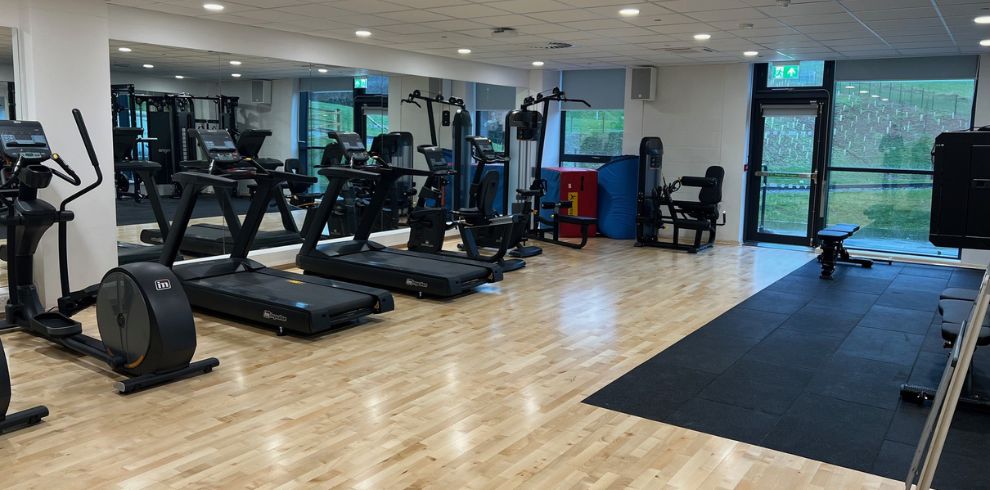 An inside gym with various equipment and shiny wooden floors.