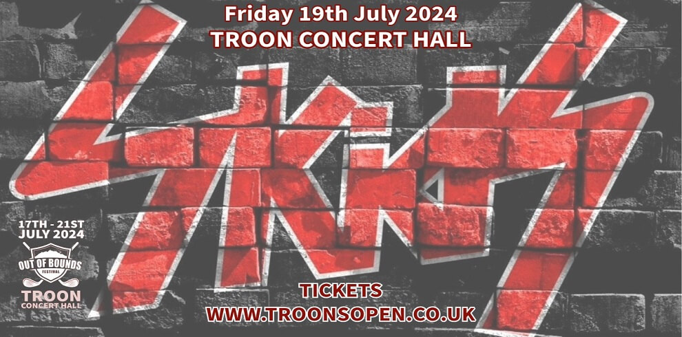 Red spray painted graffiti text sayig Skids against a black brick wall. Says Troon Concert Hall.