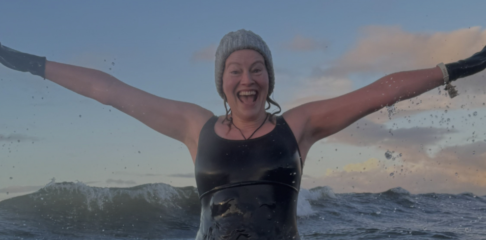 Author Chantal McFeely in the sea with her hands up in the air. She is wearing a beannie cap and swimsuit and is smiling.