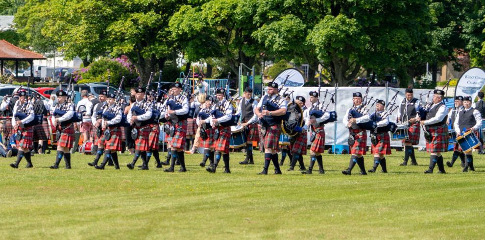 Pipers gathered in a circle in a field playing their instruments.