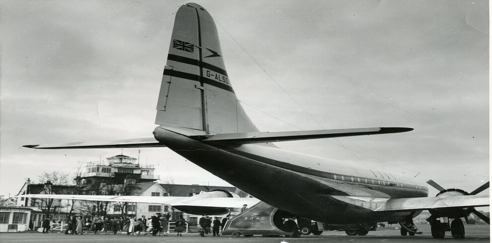 A black and white photograph captures the tail section of an airplane parked on a runway.