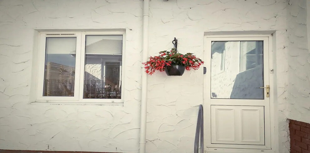 Outside of Skye Cottage. Exterior is painted white with a white door and haning basket with lovely pink flowers.