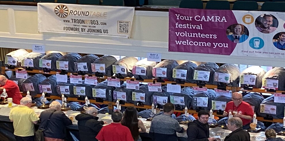 A picture of people gathered around the bar area at the Scottish Ale Festival. Behind the bar, there are numerous casks available for selection.