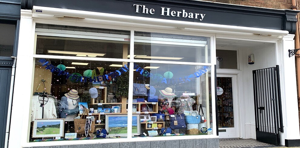 A street photo showing the shop front of The Herbary, a ladies' gift shop specialising in jewellery, bags, toiletries, and accessories. The storefront is inviting and decorated with elegant displays of various products in the window.