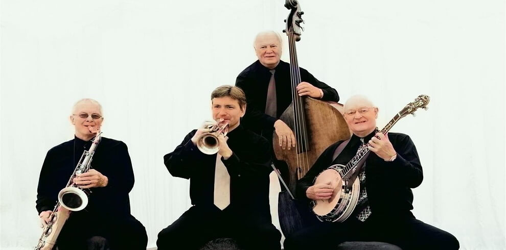 A picture of the Dixieland Jazz band performing. Four artists are playing instruments: a banjo, trumpet, saxophone, and harp.