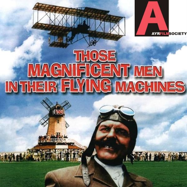 Man with large moustache wearing aviator googles and hat. A windmill in distance and old aircraft in sky.