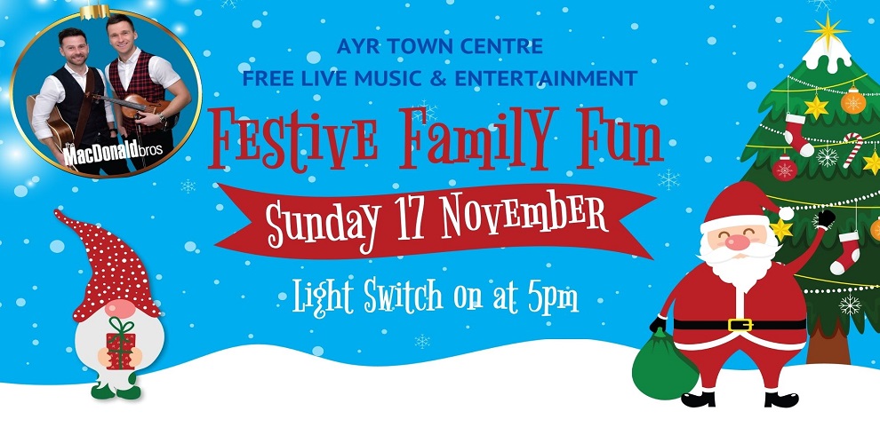 The image is a festive advertisement for an event titled "Festive Family Fun" happening at Ayr Town Centre. The design features a bright blue background with falling snow, a decorated Christmas tree, Santa Claus holding a green sack, and a cheerful elf. A red banner in the center reads "Sunday 17 November," and below it, in a festive font, "Light Switch on at 5pm" is displayed