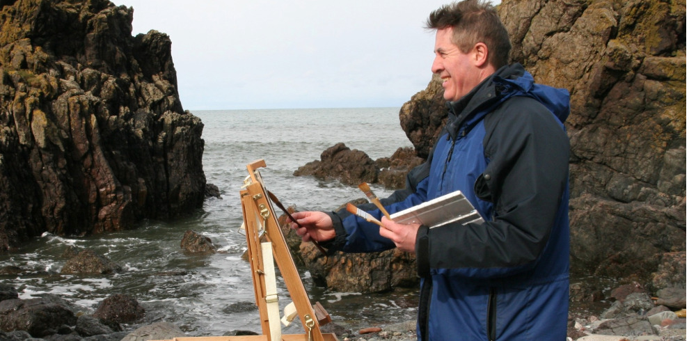 An artisit painting surrounded by rocks and sea view