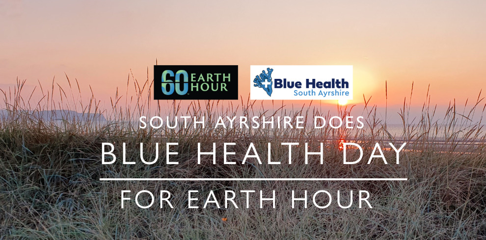 The image features a scenic coastal landscape with tall grasses in the foreground and a sunset over the water in the background. Overlaying the image are two logos: one for "Earth Hour" with a "60" in blue and black text, and another for "Blue Health South Ayrshire," which includes a blue water-themed design. The main text on the image reads: "SOUTH AYRSHIRE DOES BLUE HEALTH DAY FOR EARTH HOUR" The overall theme promotes environmental awareness and well-being in connection with Earth Hour.