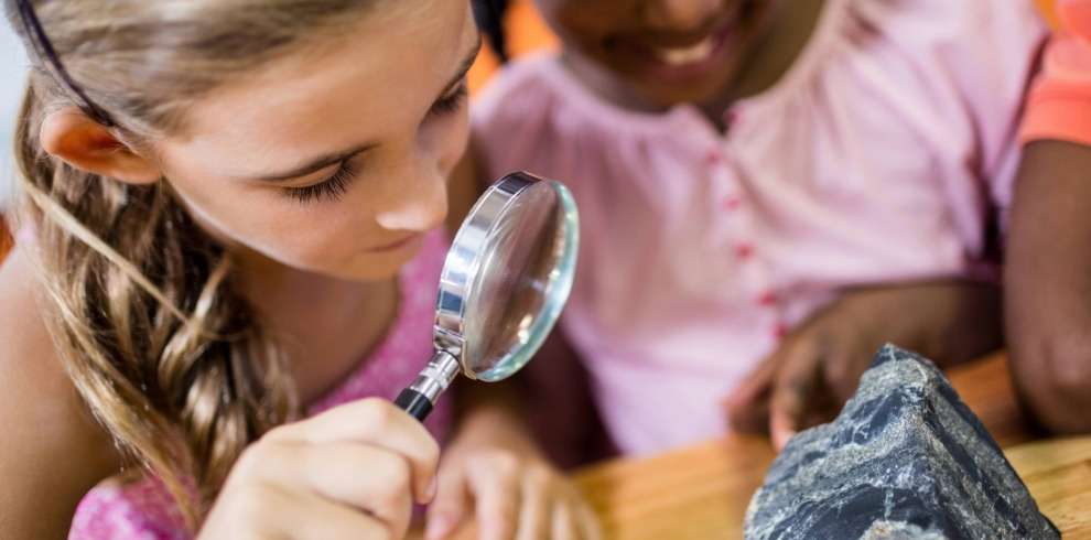 Two girls looking at a rock with a magnifying glass