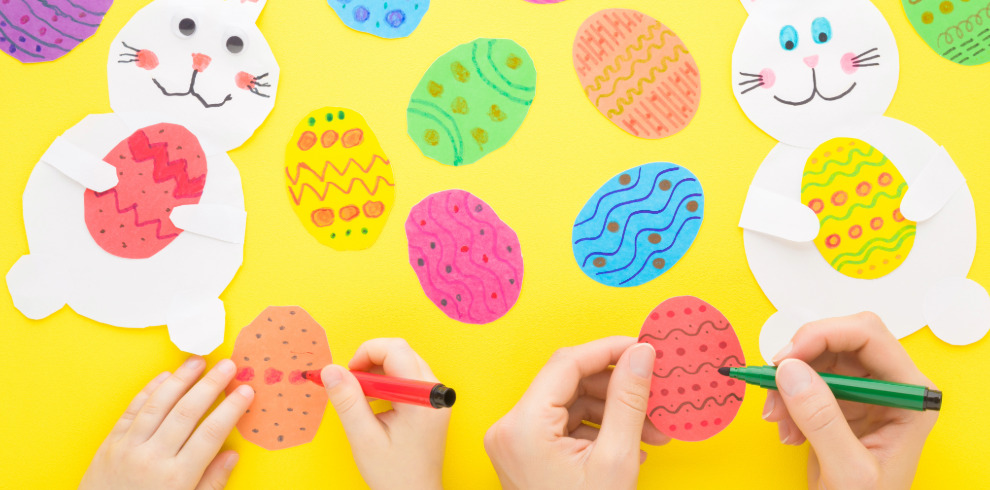 Hands colouring Easter eggs and white cut out rabbits