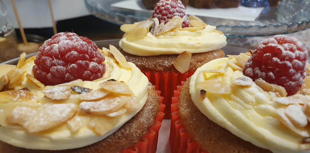 An image of three cupacakes with icingm raspberries and flaked almonds.