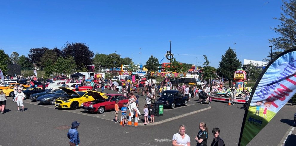 An image of an outdoor event. Classic cars and fairground attractions.