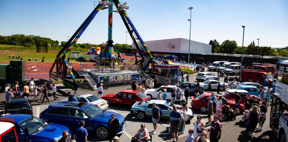 An image of an outdoor event. Classic cars and fairground attractions.