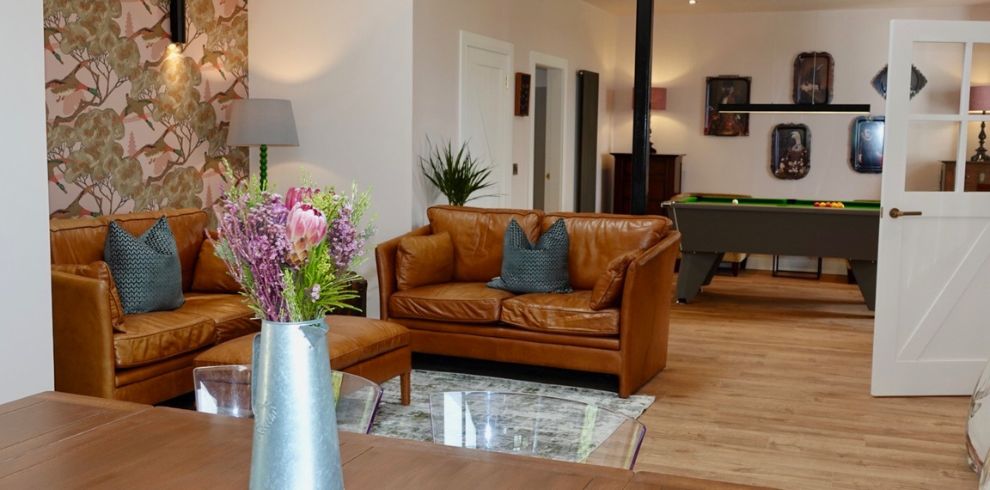 An image of a living area with sofa. In the background there is a pool table.