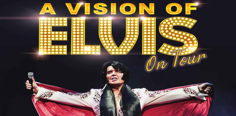 A promotional image for "A Vision of Elvis On Tour" featuring a performer dressed in a white Elvis-style jumpsuit with red and black accents, holding a microphone in one hand and spreading the cape with the other. Above the performer, large bold text reads "A VISION OF ELVIS" in bright, marquee-style lights, with "On Tour" written in a cursive font underneath. The background is dark, making the text and performer stand out.