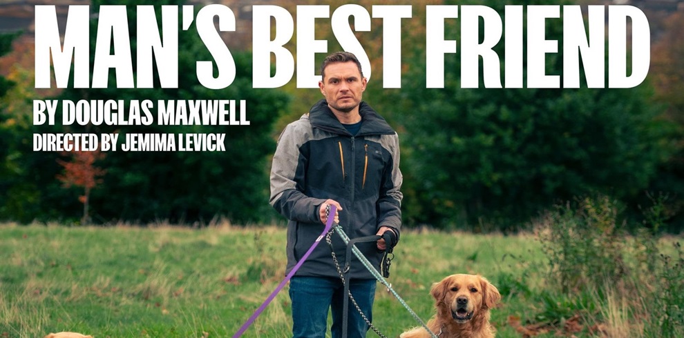 A person stands in a grassy field holding the leashes of two dogs. The person is wearing a black and gray jacket and jeans. One dog is sitting on the ground, looking at the camera, while the other dog is standing next to the person. The background consists of trees and greenery. Text in the image reads: 'MAN'S BEST FRIEND BY DOUGLAS MAXWELL DIRECTED BY JEMIMA LEVICK.'"