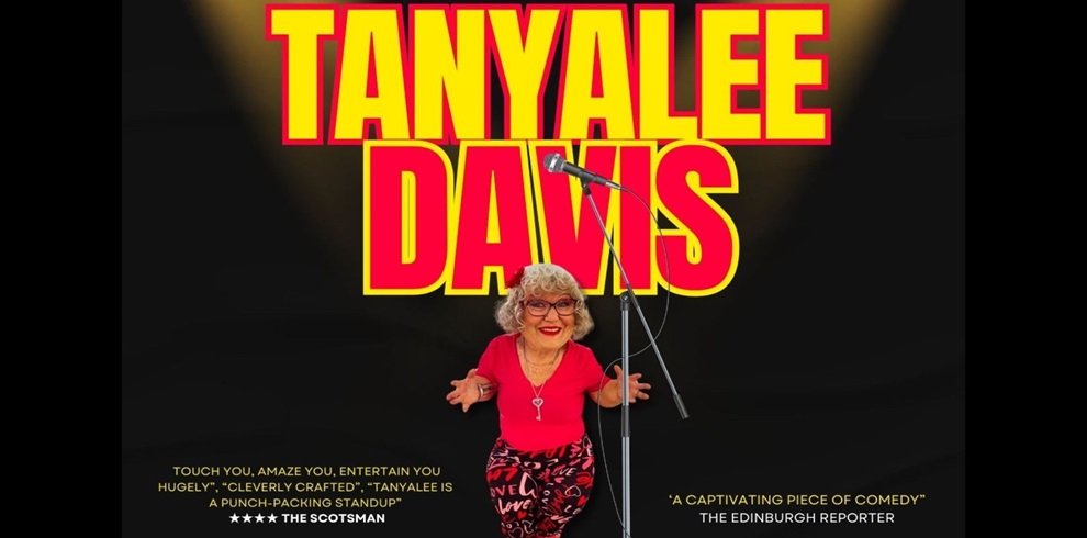 Promotional poster featuring comedian Tanyalee Davis standing in front of a large, bold text that reads "TANYALEE DAVIS" in bright red and yellow block letters. She is smiling, wearing a red top and patterned red-and-black pants, standing behind a microphone stand. Below her are two quotes: one from The Scotsman that reads, "Touch you, amaze you, entertain you hugely," and another from The Edinburgh Reporter that calls her "a captivating piece of comedy." The background is dark with a spotlight effect highlighting Tanyalee.