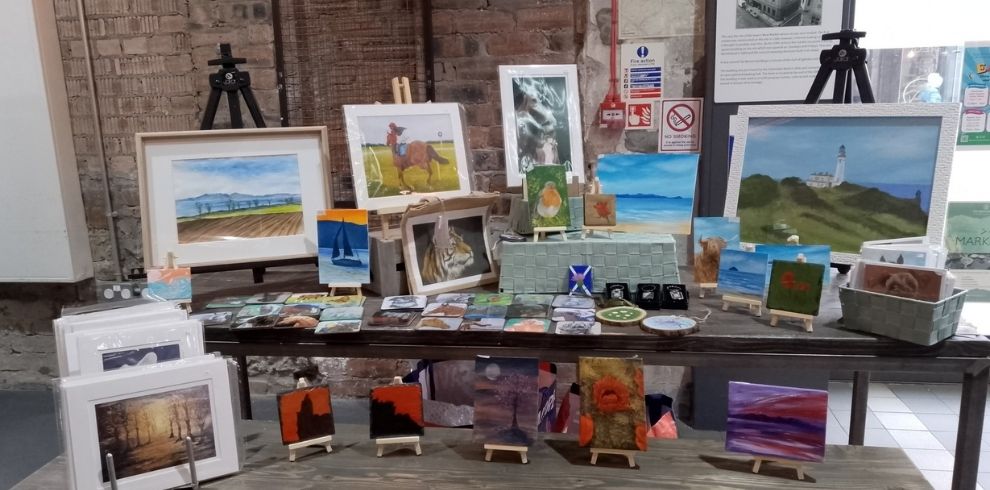A stall with paintings and crafts in a market environment.