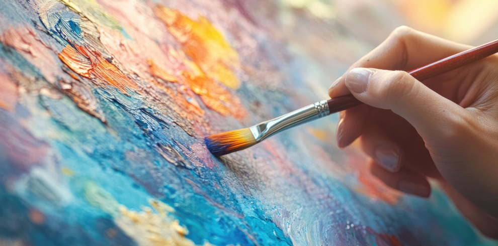 Image of a hand holding a paintbrush, painting on a canvas.